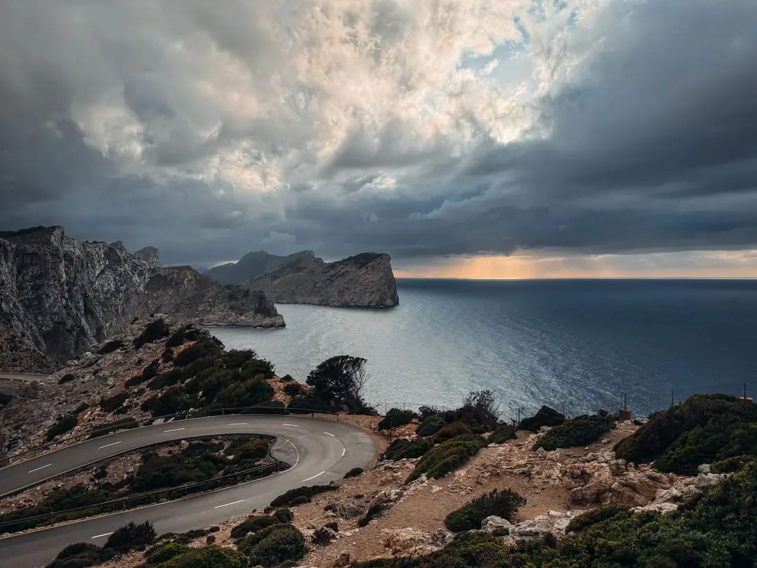 Captivating coastal road view in Mallorca, Spain with dramatic cliffs and sea under a cloudy sky.