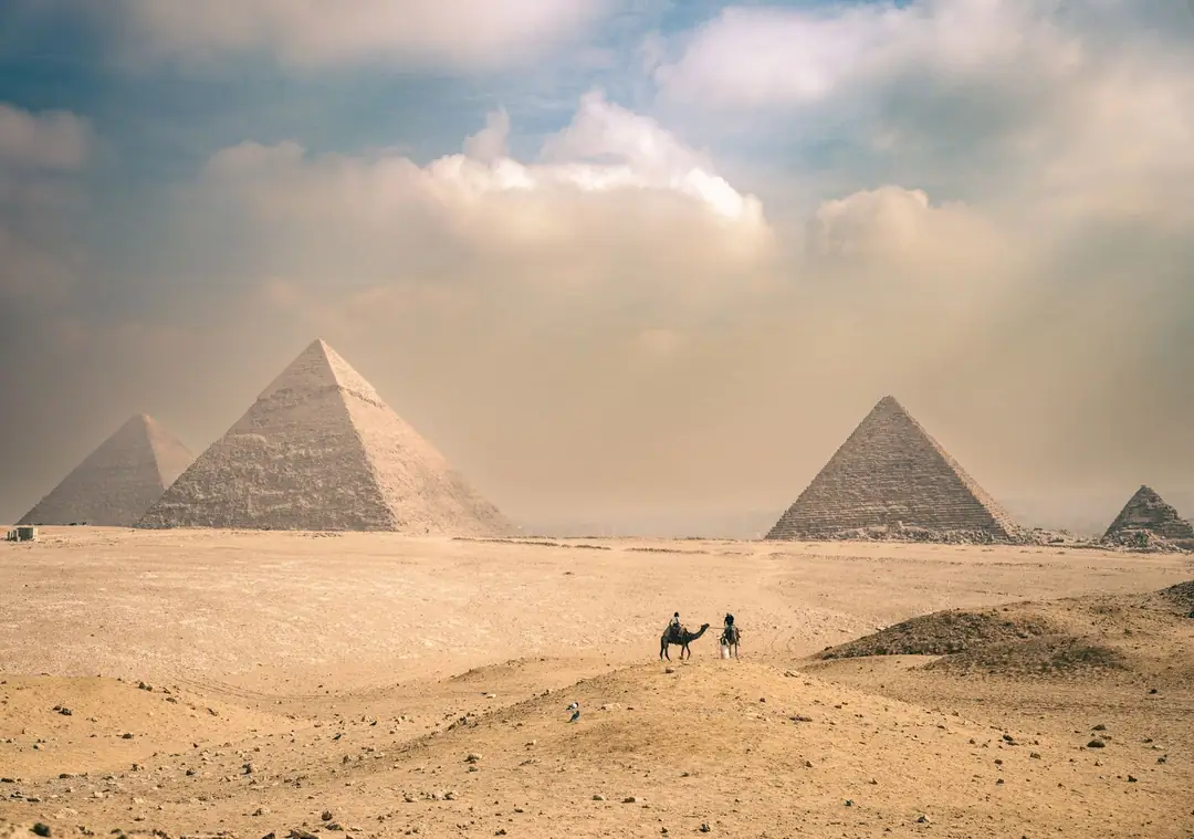 Explore the majestic Pyramids of Giza under a sunny sky with distant travelers on camels.