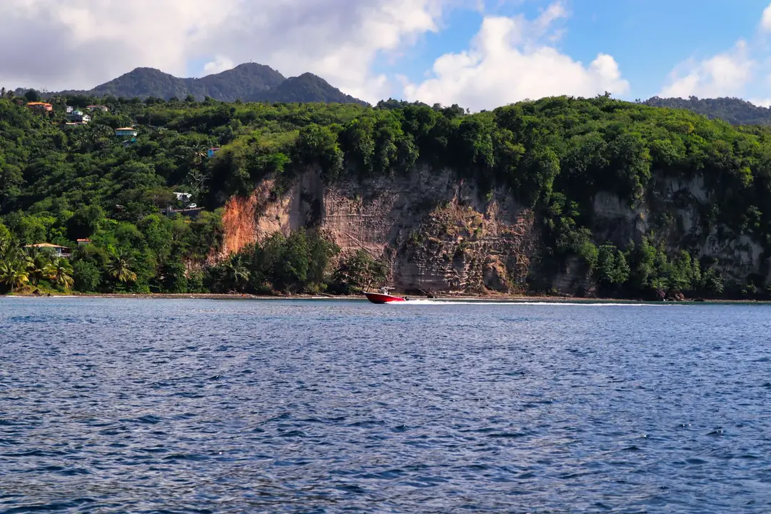 A speed boat cruising along the coastline of Saint Lucia with lush green cliffs and mountains in the background.