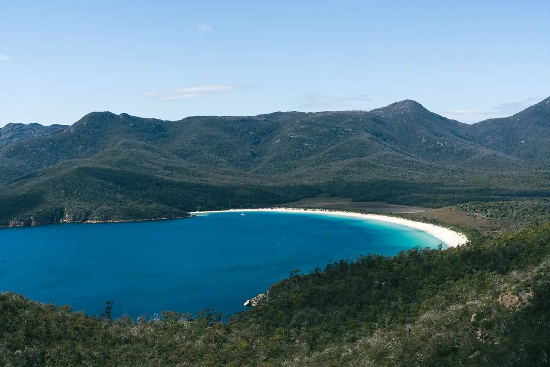 A breathtaking aerial view of Wineglass Bay's turquoise waters and lush surrounding mountains in Tasmania.